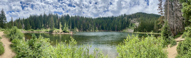 panoramic photo of lake surrounded by trees and blue sky